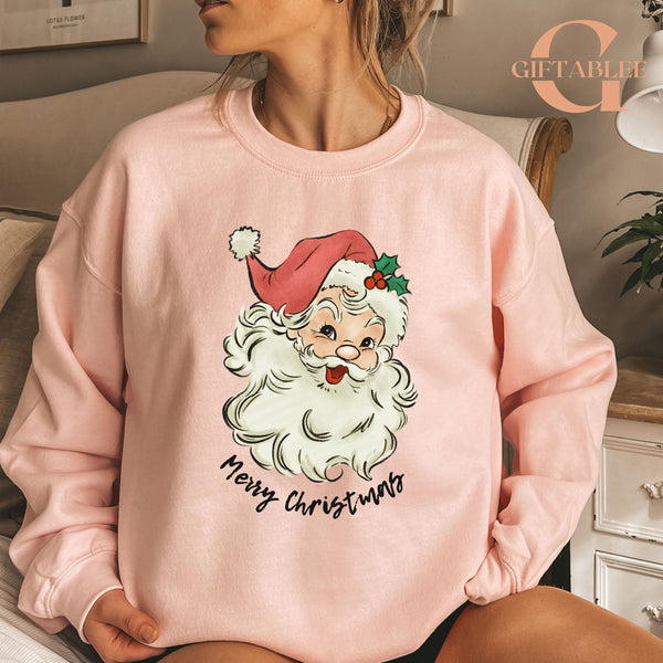 A woman wearing a pink sweatshirt with a Santa Claus design and the text "Merry Christmas" printed on it.