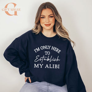 A woman wearing a navy blue sweatshirt with the text "I'M ONLY HERE TO ESTABLISH MY ALIBI" printed on it.