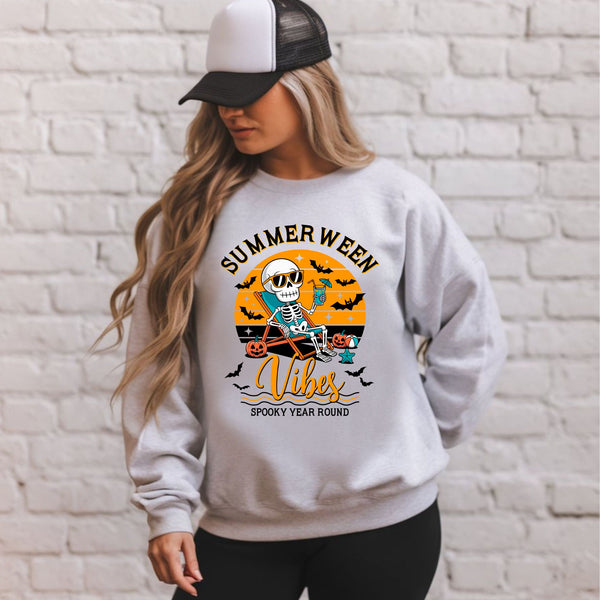 A woman wearing a gray sweatshirt with a graphic design featuring a skeleton riding a skateboard and the text "Summer Ween Vibes Spooky Year Round".
