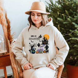 A woman wearing a white hoodie with a Halloween-themed graphic stands in front of a Christmas tree.