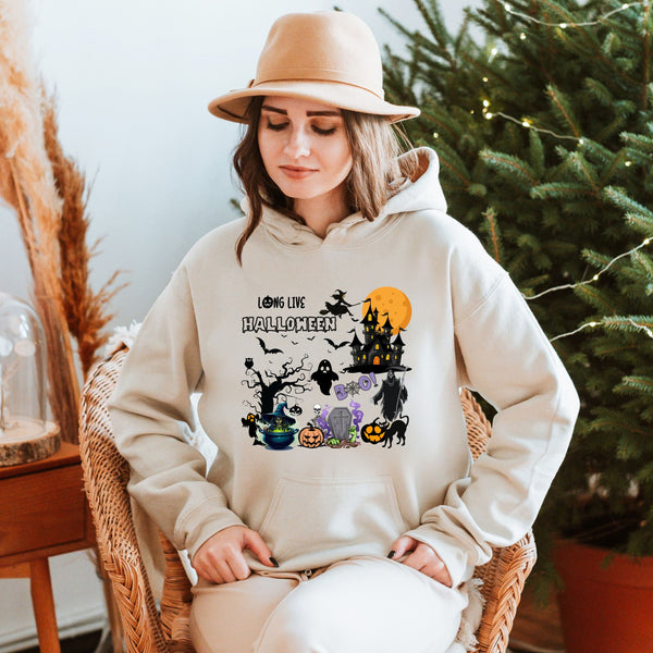 A woman wearing a white hoodie with a Halloween-themed graphic stands in front of a Christmas tree.