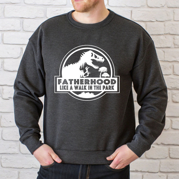 A man wearing a gray sweatshirt with a graphic design featuring a dinosaur and the text "FATHERHOOD LIKE A WALK IN THE PARK".