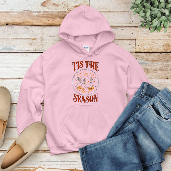 A pink hoodie with a graphic design and text printed on it, along with a pair of jeans and a pair of shoes, all laid out on a wooden surface.