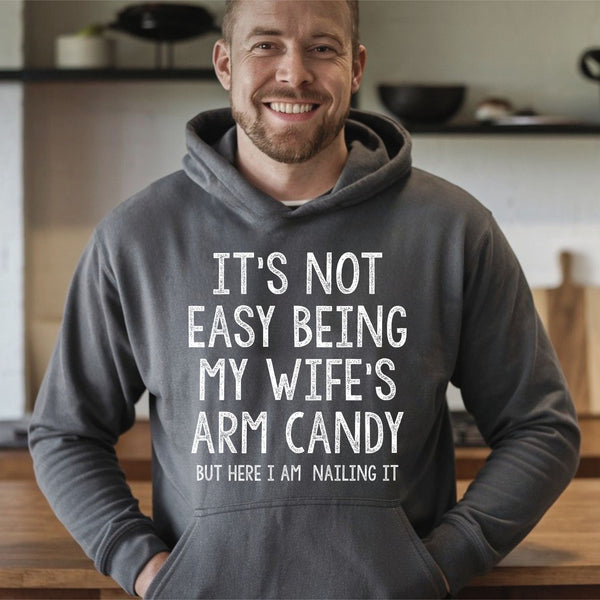 A man wearing a grey hoodie with a humorous text printed on it, smiling at the camera.
