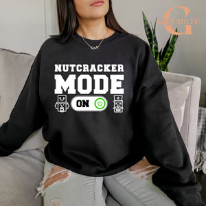 A woman wearing a black sweatshirt with the text "NUTCRACKER MODE ON" printed on it.