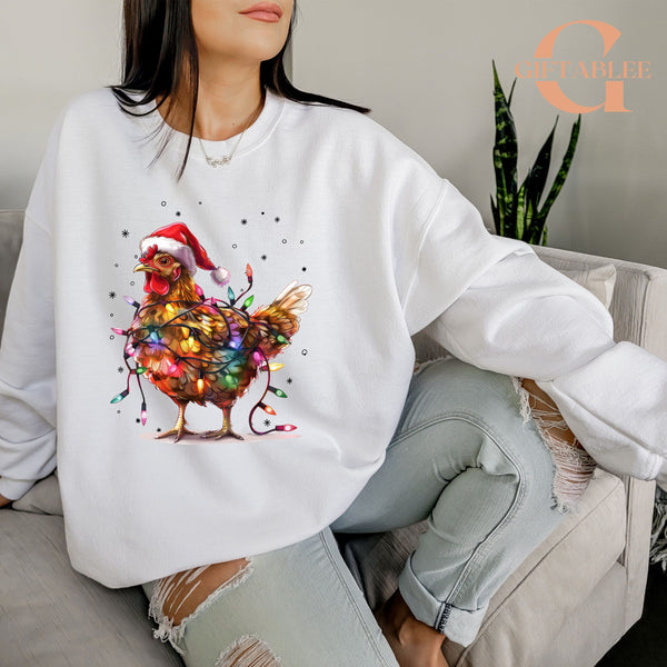 A woman wearing a white sweatshirt with a colorful illustration of a chicken wearing a Santa hat and surrounded by Christmas lights.