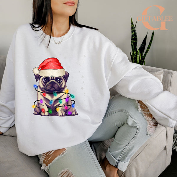 A woman wearing a white sweatshirt with a graphic of a pug wearing a Santa hat and Christmas lights.