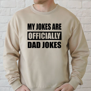 A man wearing a beige sweater with the text "MY JOKES ARE OFFICIALLY DAD JOKES" printed on it.