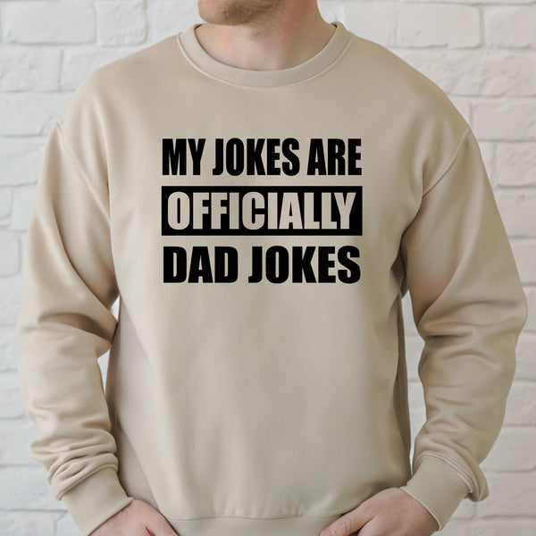 A man wearing a beige sweater with the text "MY JOKES ARE OFFICIALLY DAD JOKES" printed on it.