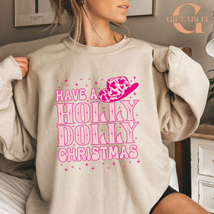 A woman wearing a beige sweatshirt with a pink and white design that says "Have a Holly Dolly Christmas".