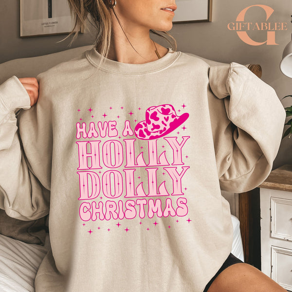 A woman wearing a beige sweatshirt with a pink and white design that says "Have a Holly Dolly Christmas".