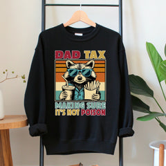 A black sweatshirt with a graphic design depicting a raccoon wearing sunglasses and holding a cup of fries, along with the text "DAD TAX MAKING SURE IT'S NOT POISON".
