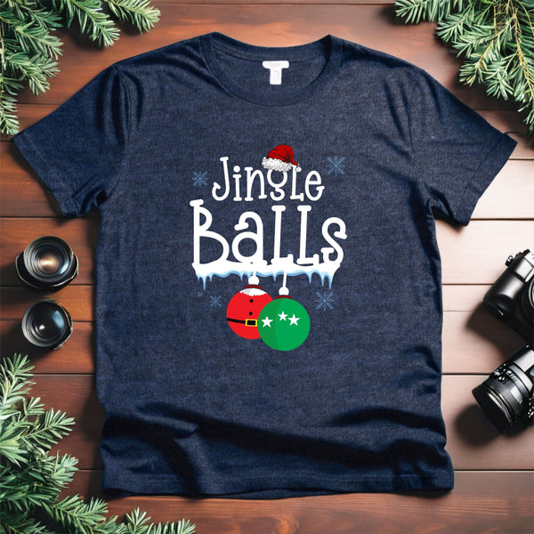 A navy blue t-shirt with a humorous text design that reads "Jingle Balls" and features a Santa hat and Christmas ornaments. The t-shirt is placed on a wooden surface, surrounded by holiday decorations such as pine branches.