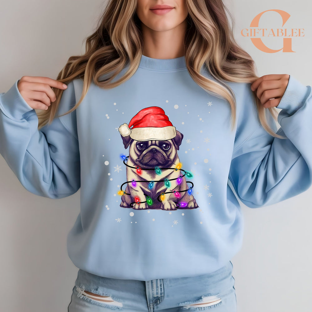 A woman wearing a light blue sweatshirt with a graphic of a pug wearing a Santa hat and surrounded by colorful Christmas lights.