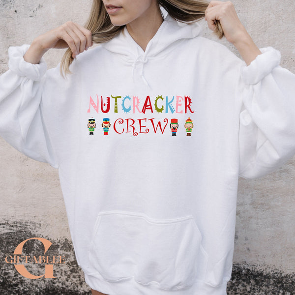 A woman wearing a white hoodie with the text "NUTCRACKER CREW" printed on it.