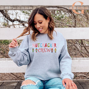 A woman wearing a grey sweatshirt with the text "NUTS CREW" printed on it, sitting on a bench and smiling.