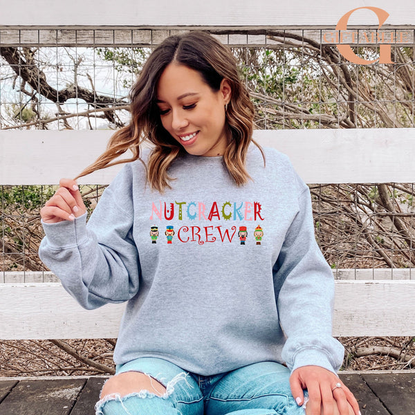 A woman wearing a grey sweatshirt with the text "NUTS CREW" printed on it, sitting on a bench and smiling.