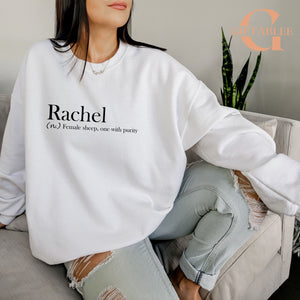 A woman wearing a white sweatshirt with the word "Rachel" printed on it, sitting on a couch.