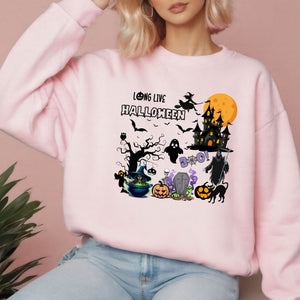 A woman wearing a pink sweatshirt with a Halloween-themed graphic design featuring various spooky and festive elements such as a castle, bats, a ghost, a witch's hat, a pumpkin, and a spider.