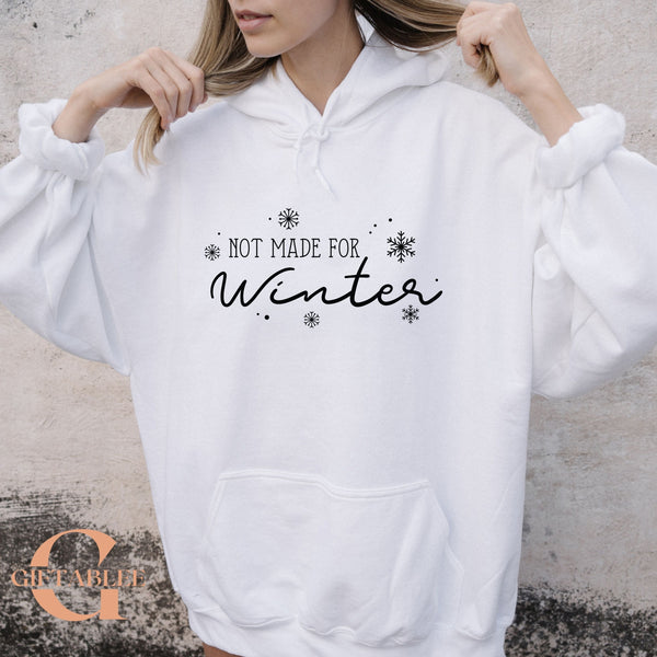 A woman wearing a white hoodie with the text "NOT MADE FOR WINTER" printed on it.