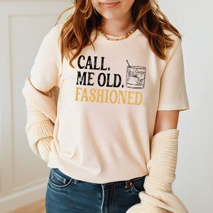 A woman wearing a white t-shirt with the text "Call me old, fashioned" printed on it, along with a graphic of a glass of alcohol.