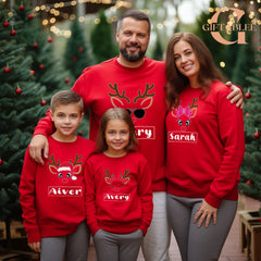 A family of four, consisting of two parents and two children, is posing for a photo in red Christmas sweaters with reindeer designs.