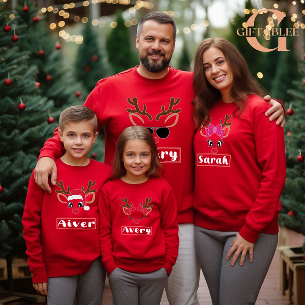 A family of four, consisting of two parents and two children, is posing for a photo in red Christmas sweaters with reindeer designs.