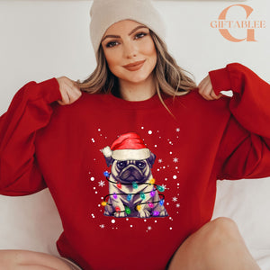 A woman wearing a red sweater with a pug dog wearing a Santa hat and surrounded by Christmas lights.