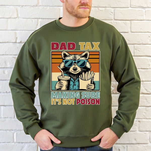 A man wearing a green sweatshirt with a graphic design featuring a raccoon wearing sunglasses and holding a drink, along with the text "DAD TAX MAKING SURE IT'S NOT POISON".