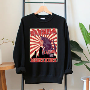 A black sweatshirt with a graphic design featuring a large image of a Godzilla-like creature and the text "DADZILLA, FATHER OF MONSTERS" printed on it.