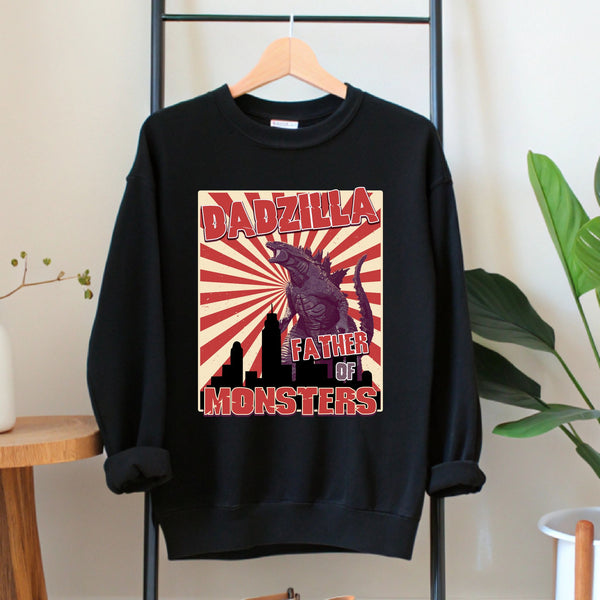 A black sweatshirt with a graphic design featuring a large image of a Godzilla-like creature and the text "DADZILLA, FATHER OF MONSTERS" printed on it.
