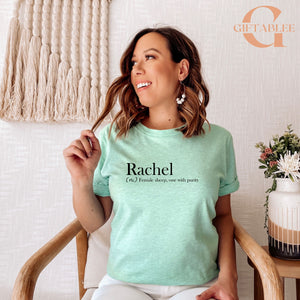 A woman wearing a mint green t-shirt with the word "Rachael" printed on it, smiling and looking to the side.