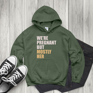A green hoodie with text printed on it, along with a pair of black and white sneakers, placed on a wooden surface.