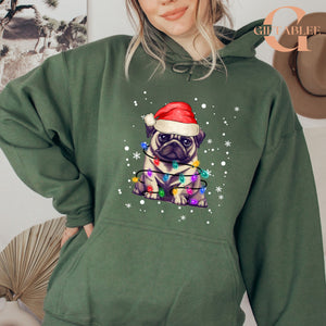 A woman wearing a green hoodie with a graphic of a pug wearing a Santa hat and surrounded by Christmas lights.