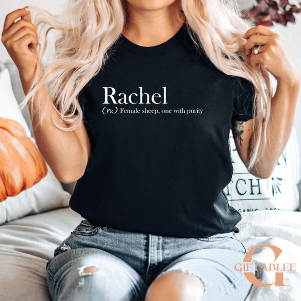 A woman with long blonde hair wearing a black t-shirt with the word "Rachel" printed on it, sitting on a couch.