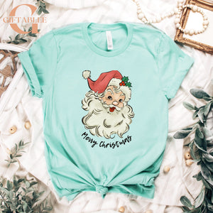 A turquoise t-shirt with a Santa Claus graphic and the text "Merry Christmas" printed on it, along with some greenery and beads.