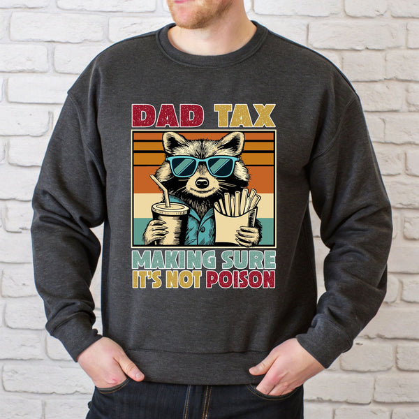 A man wearing a gray sweatshirt with a graphic design featuring a raccoon wearing sunglasses and holding a drink, along with the text "DAD TAX MAKING SURE IT'S NOT POISON".