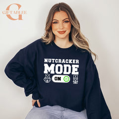 A woman wearing a navy blue sweatshirt with the text "NUTCRACKER MODE ON" printed on it.