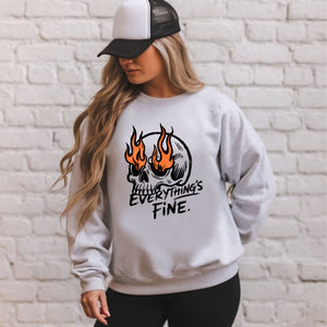 A woman wearing a gray sweatshirt with a graphic design of a skull with flames on it, and the text "Everything's Fine" printed on it.