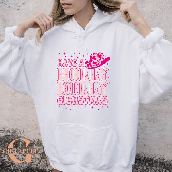 A woman wearing a white hoodie with a pink and white design that says "Have a Holly Dolly Christmas".