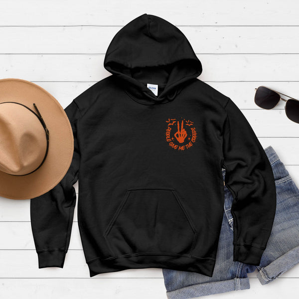 A black hoodie with an orange graphic, a tan hat, sunglasses, and a pair of blue jeans are arranged on a white wooden surface.