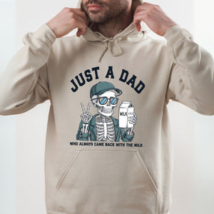 A man wearing a beige hoodie with a graphic design of a skeleton wearing sunglasses and holding a carton of milk, along with the text "Just a Dad" and "Who always came back with the milk".