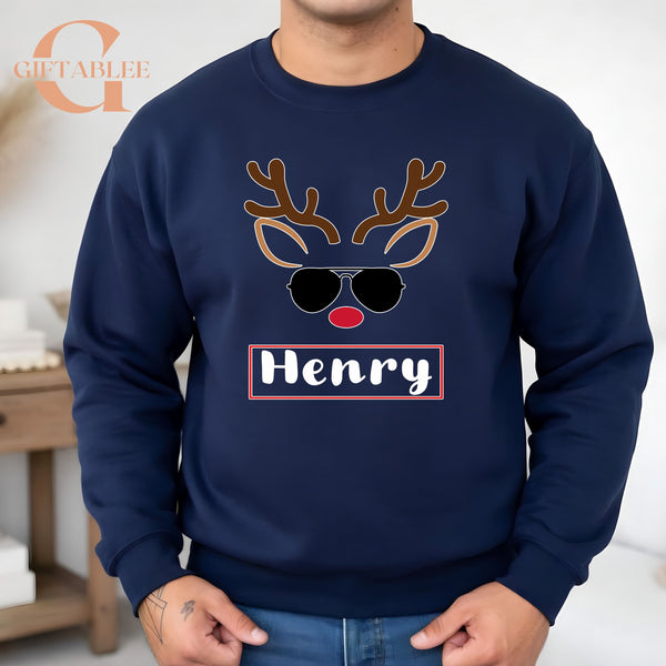 A man wearing a navy blue sweater with a graphic design of a reindeer wearing sunglasses and the name "HENRY" printed on it.