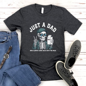 A gray t-shirt with a graphic design of a skeleton wearing sunglasses and holding a carton of milk, accompanied by the text "Just a Dad" and "Who always came back with the milk".
