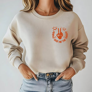 A woman wearing a beige sweater with an orange graphic design on the front, which appears to be a peace sign.