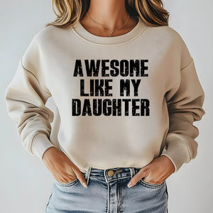 A woman wearing a beige sweatshirt with the text "AWESOME LIKE MY DAUGHTER" printed on it.