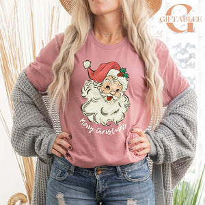 A woman wearing a pink t-shirt with a Santa Claus graphic and the text "Merry Christmas" stands in front of a window.